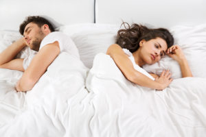 Upset young couple having disagreement lying side by side in bed facing in opposite directions